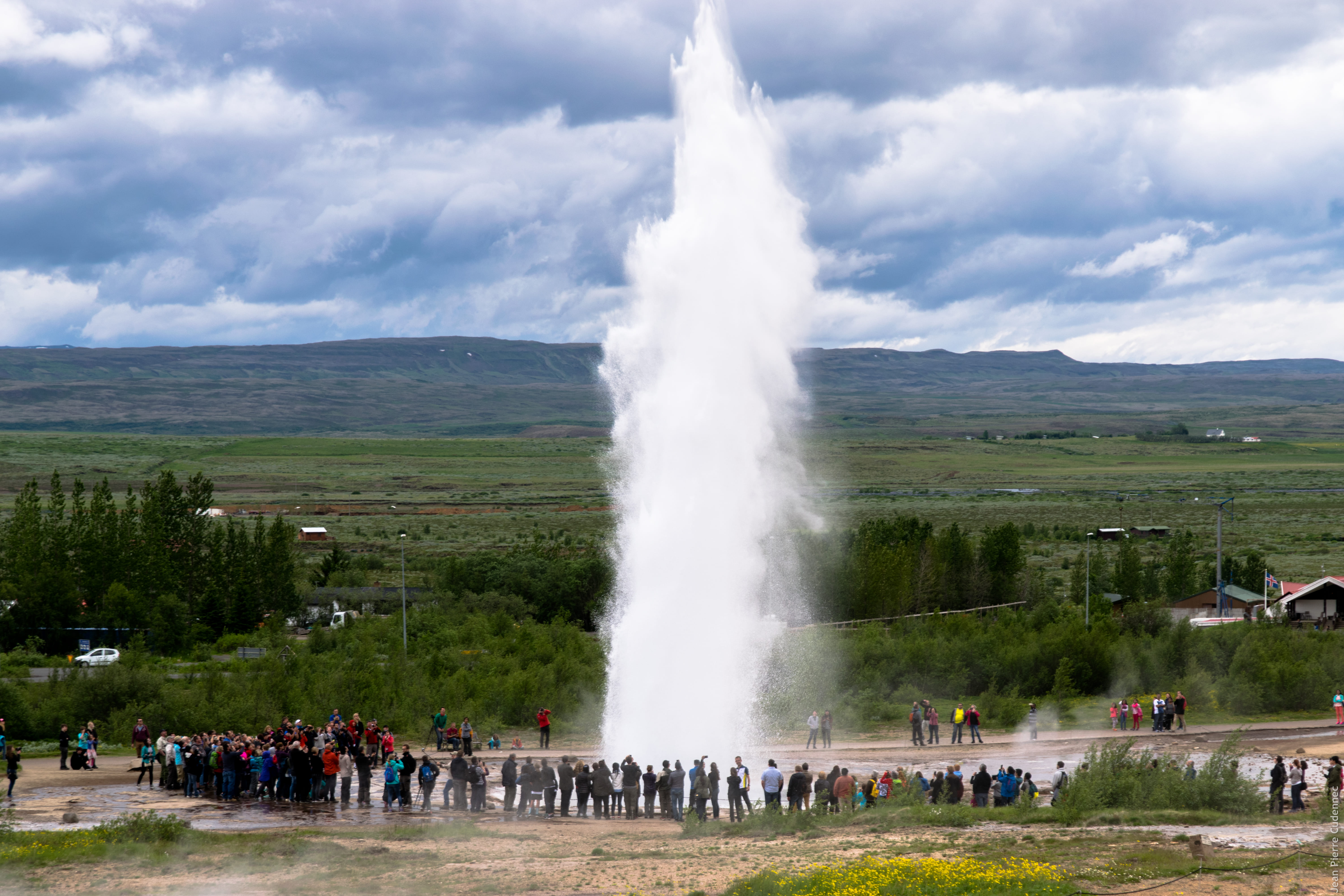 People looking at Strokkur geyser against cloudy sky