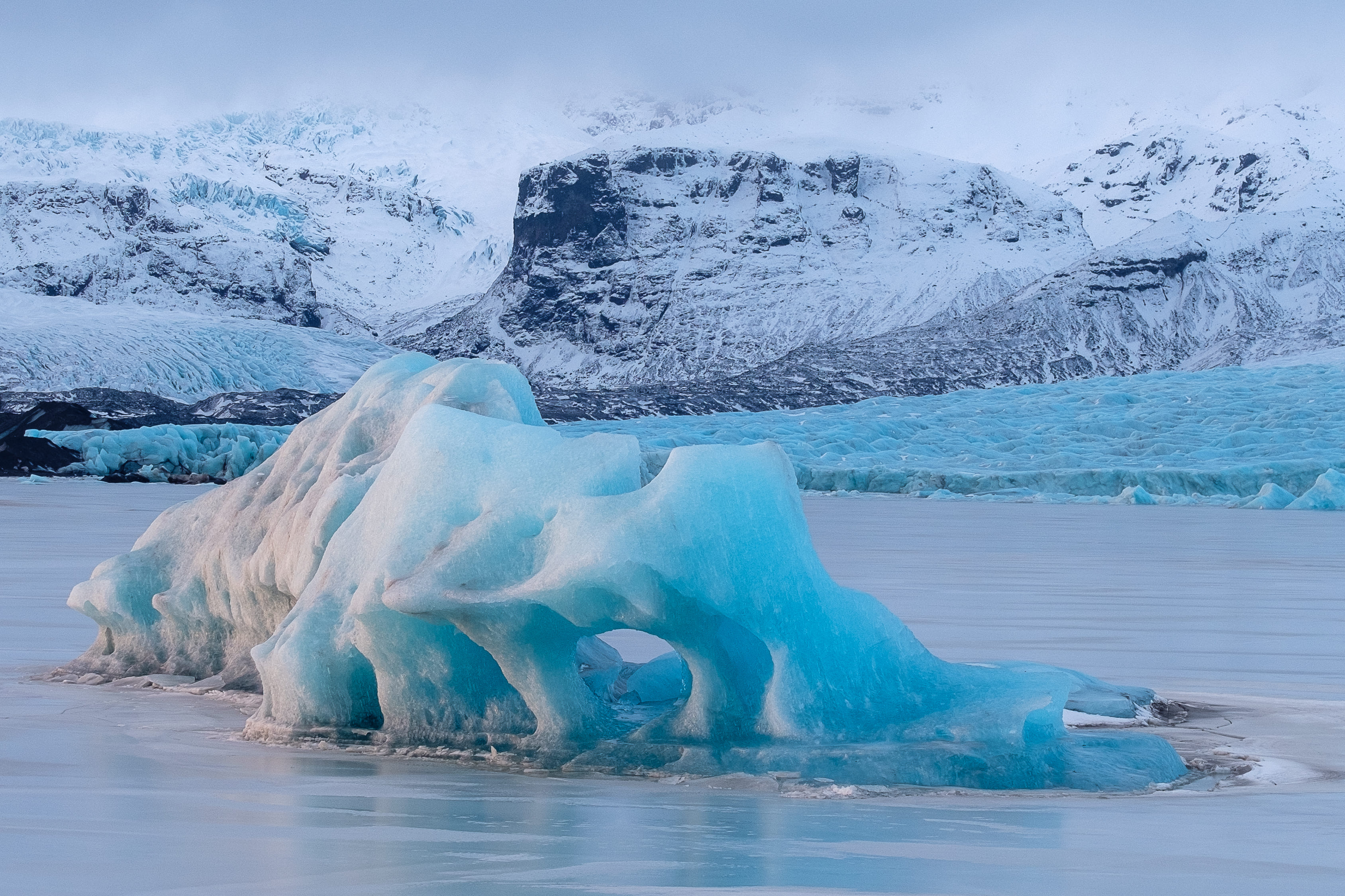 Iceland - blue iceberg in the middle of a lake with magnificent mountains at the background
